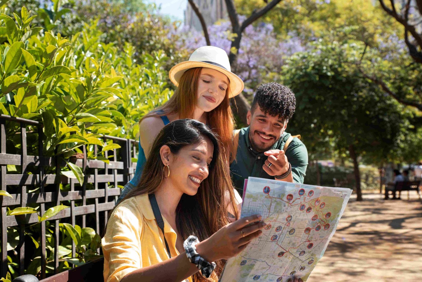 Jovens turistas consultando mapa turístico com guia de turismo profissional em ambiente urbano arborizado
