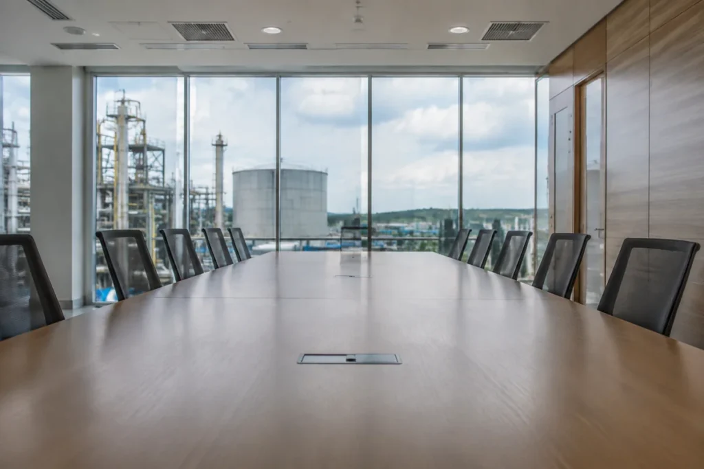 Mesa de reunião vazia em escritório sóbrio com vista para pátio industrial.