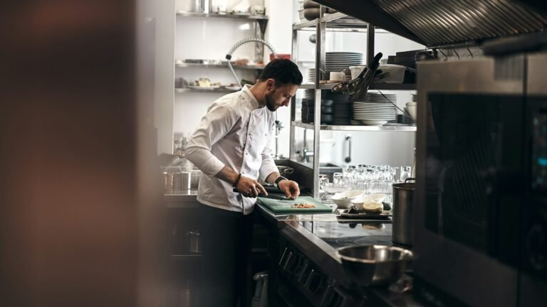 Chef de jaleco branco cortando legumes em cozinha profissional